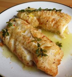 two fish fillets on a white plate with lemon sauce and parmesan cheese