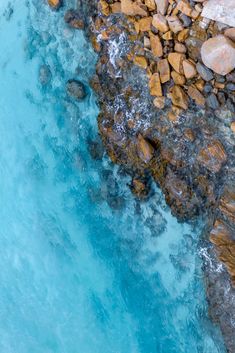 an aerial view of the ocean with rocks and blue water in the foreground, from above