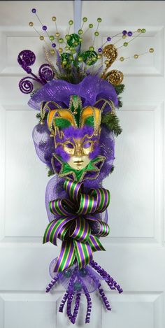 a mardi gras mask hanging on a door with purple and green streamers