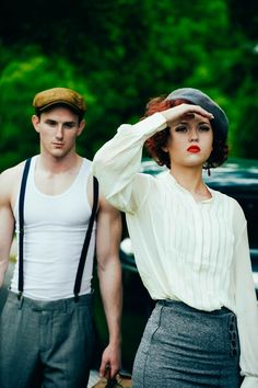 a man and woman standing next to each other in front of a green car with trees behind them