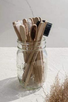 several wooden toothbrushes in a glass jar on a white counter top next to dried grass