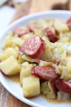 a white plate topped with sausage and potatoes on top of a wooden table next to a fork