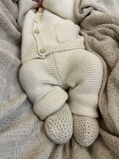 a baby is laying on top of a blanket and wearing a white sweater with buttons