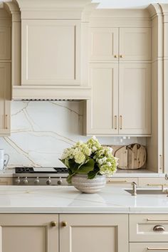 a white kitchen with marble counter tops and cabinets in the background is a vase filled with flowers