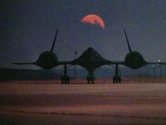 an air force jet sitting on top of an airport tarmac under a red moon