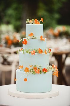 a three tiered cake with orange flowers on the top is sitting on a table