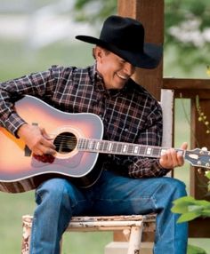 a man with a cowboy hat playing an acoustic guitar on a chair in the yard