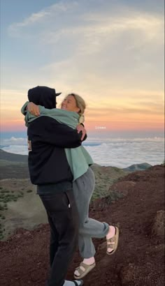 two people hugging each other on top of a hill