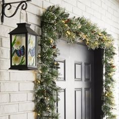 a white brick wall with a black door and green garland on the front, next to a lantern light