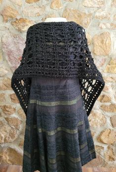 a black crochet sweater on a mannequin head stand in front of a stone wall