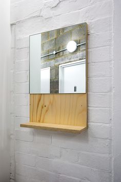 a mirror mounted to the side of a white brick wall next to a wooden shelf