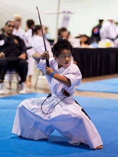 a young boy is practicing karate on the blue carpet in front of an audience with other people watching