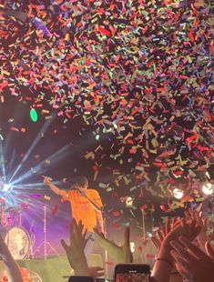 people are holding their hands up in front of confetti on the ceiling at a concert