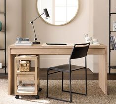 a desk with a chair, lamp and bookshelf in front of a round mirror