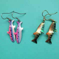 three different colored fish shaped earrings on a blue background