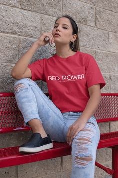 a woman sitting on a red bench next to a brick wall wearing a red power t - shirt