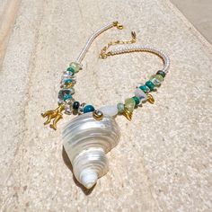 The Corsica Necklace is a playful summer statement that reflects the delights of the beach. It’s hand-assembled with freshwater pearls, semi-precious beads of varying sizes and shapes, and golden charms—all to complement the centerpiece. Adorned with a bezel-set crystal, the swirly turbo shell has an alluring iridescence that’s hard to resist. Beach Jewelry With Pearl And Gemstone Beads, Beach Pearl Jewelry With Gemstone Beads, Beach Pearl Necklace With Natural Stones, Pearl Jewelry With Gemstone Beads For Beach, Beach Baroque Pearl Jewelry With Pearl Charm, Pearl White Beach Necklace With Pearl Charm, Beach Necklace With Natural Stones And Pearls, Pearl White Necklace With Pearl Charm For Beach, Pearl Beaded Necklace With Gemstone Beads For Beach