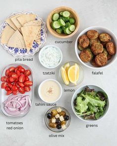 the ingredients for this salad are shown in bowls, including pita bread, cucumbers, tomatoes, lettuce, olives, and lemon