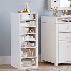 a white cabinet with lots of items on it next to a mirror and dresser in a room