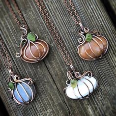 three necklaces with different designs on them sitting on a wooden surface, one has a pumpkin and the other has a green leaf