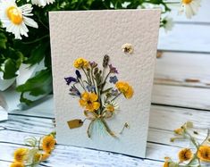 a white card with yellow and purple flowers on it, next to some daisies