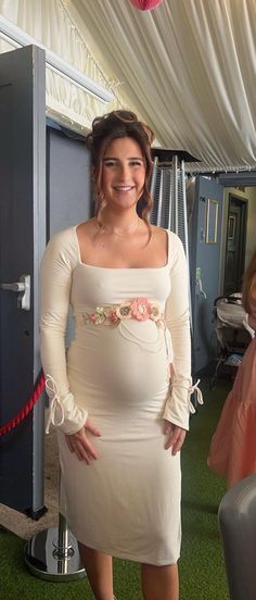 a pregnant woman in a white dress standing next to a pink ballon shaped object