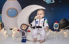 a baby sitting on the moon with an astronaut doll next to it in front of a rocket ship backdrop