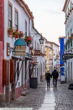 two people walking down a cobblestone street in an old european town, holding hands