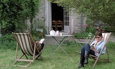 two people sitting in lawn chairs reading books