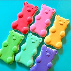 four different colored teddy bear cookies on a blue table top with green, yellow, pink and purple frosting