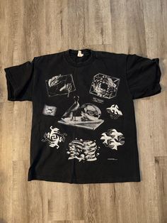 a black t - shirt with various images on it sitting on a wooden floor next to a pair of scissors