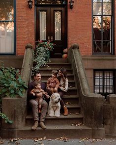 three people sitting on the steps with their dog in front of an apartment building that has stairs leading up to it