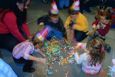 a group of children sitting around a table with party hats on top of them and confetti all over the floor