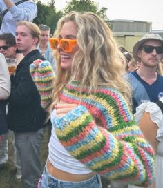 a woman wearing colorful knitted sweater and sunglasses standing in front of a group of people