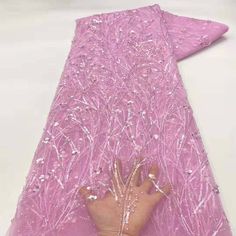 a person's hand is touching the back of a pink piece of cloth with white beads on it