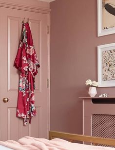 a bedroom with pink walls and clothes hanging on the door, next to a bed