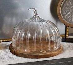 a clear glass cake dish sitting on top of a wooden stand next to a clock