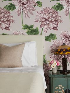 a bed with pink flowers on the wall next to a night stand and side table