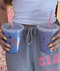 a woman is holding two cups with straws in her hands and wearing sweatpants