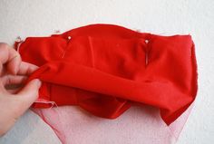 someone is stitching the fabric on top of a red piece of cloth with scissors