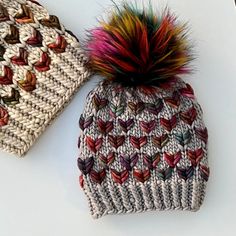 two knitted beanies with multi colored pom - poms on white surface