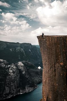 a man standing on top of a cliff next to a body of water in the distance