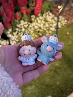 two little pigs are in the palm of someone's hand with flowers behind them