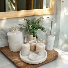 marble bathroom accessories displayed on wooden tray in front of large mirror and potted plant