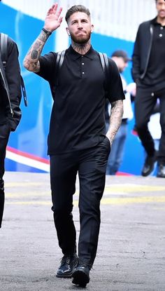 a man walking down the street with his hand up in the air while wearing all black