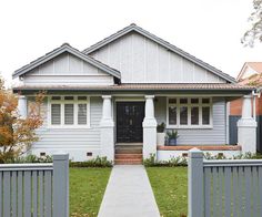 a gray house with white trim on the front door and side porch, along with a grey picket fence