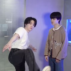 two young men standing next to each other in front of a wall with an aquarium