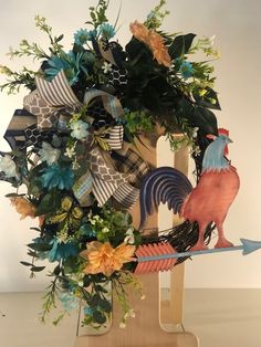 a wooden stand holding a wreath with flowers and roosters on it's sides