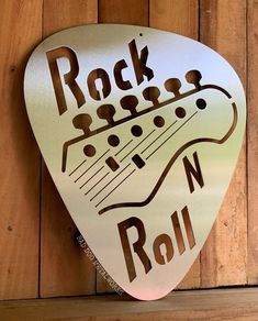 a metal guitar picker with the words rock n roll on it hanging from a wooden wall