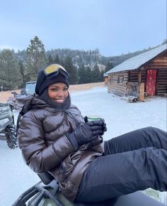 a woman sitting on top of a snow covered ski slope next to a log cabin